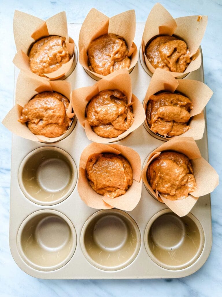 Pumpkin batter has been poured into a paper-lined muffin pan and is reading for baking in the oven.