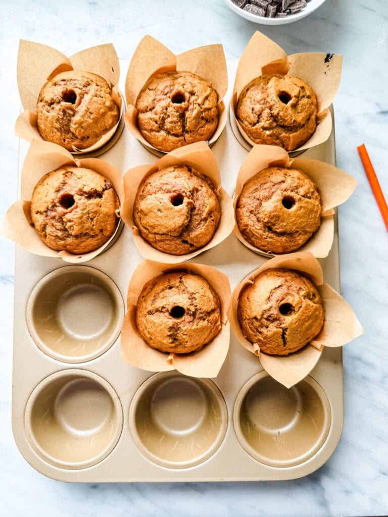 A tray of eight pumpkin spice muffins. Each muffin has a hole in the center. The hole will be filled with molten chocolate.