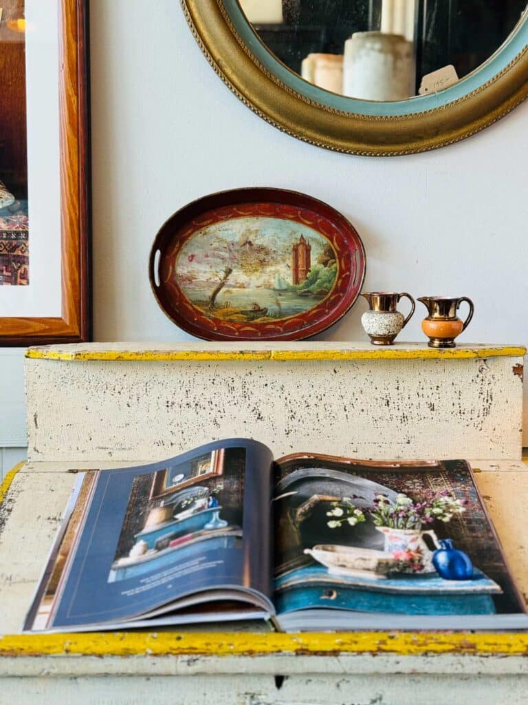 book open on distressed table with shelf, oval platter, 2 small pitchers 