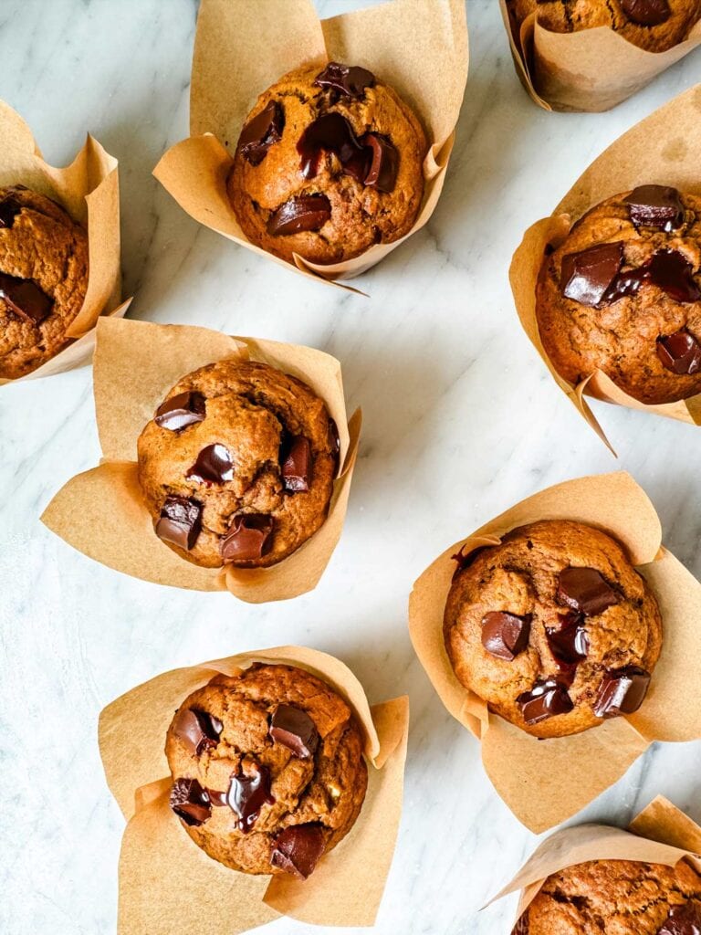 Pumpkin spice muffins with molten chocolate are wrapped in paper and sitting on a kitchen counter.