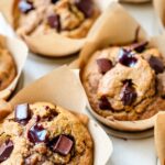 Paper-wrapped pumpkin muffins filled with molten chocolate are sitting on a kitchen counter.