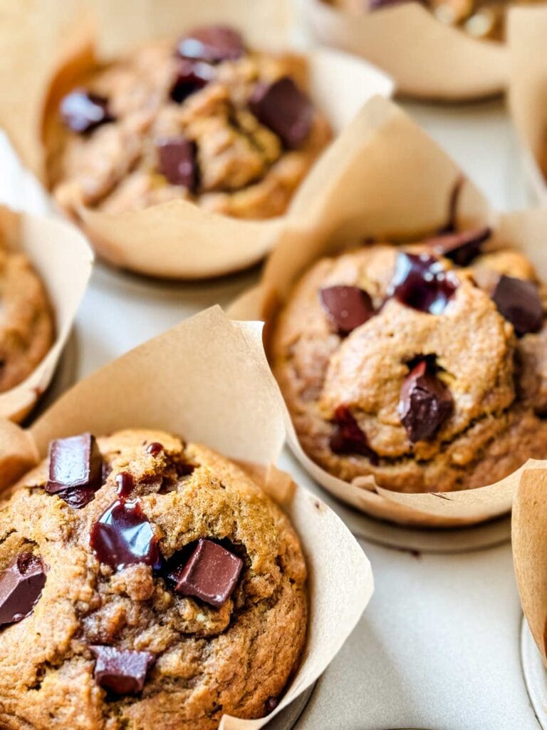 Paper-wrapped pumpkin muffins filled with molten chocolate are cooling on a kitchen counter.