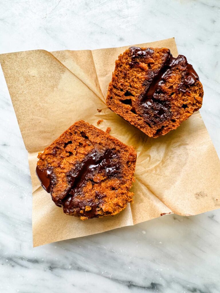 A pumpkin spice muffin with molten chocolate has been sliced in half and is sitting on a paper muffin wrapper.