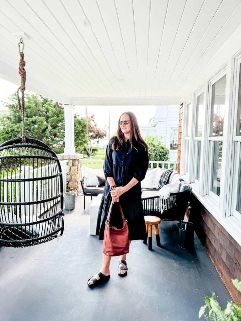 Woman wearing black dress and sungleasses on a porch.