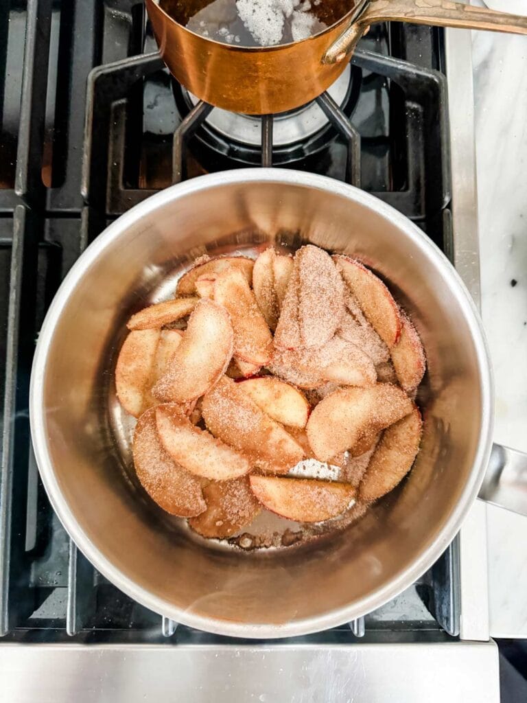 Sliced apples, sugar, and cinnamon are cooking in a pot on the stove.