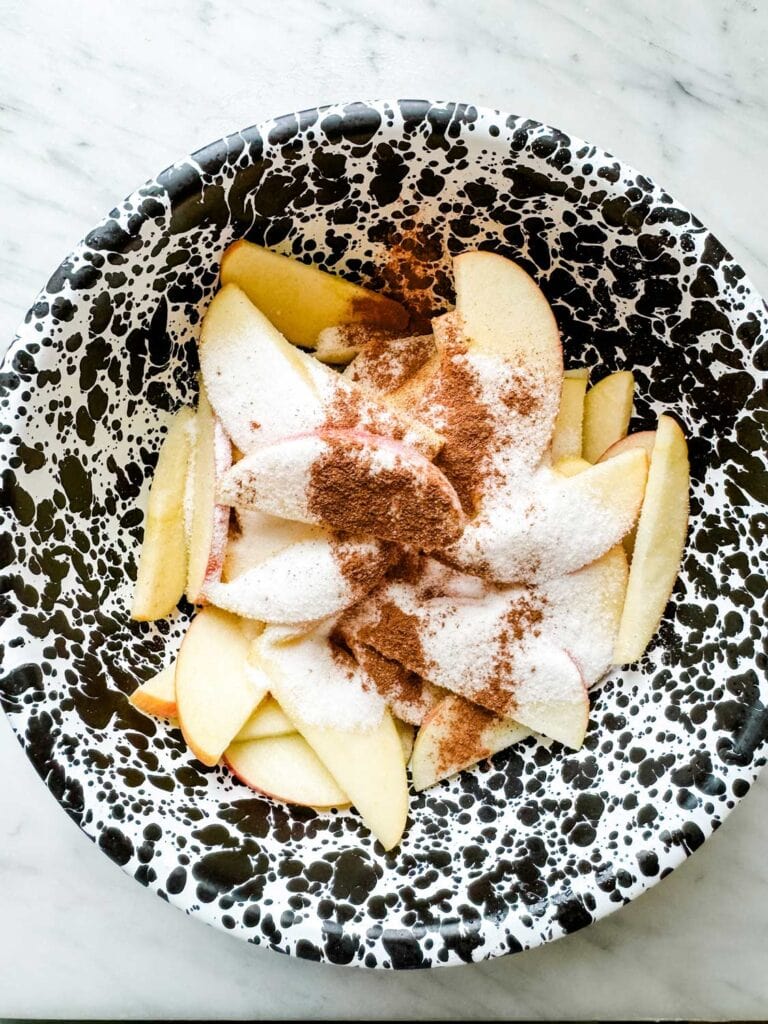 Apple slices are in a mixing bowl and sugar and brown cinnamon have been added.