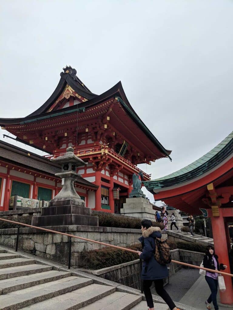 A red temple in Japan, woman walking up the steps holding a railing