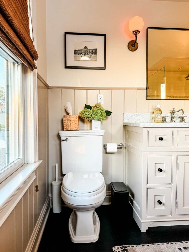 White toilet, hydrangeas, seagrass tissue box cover, sconce, framed photograph. 