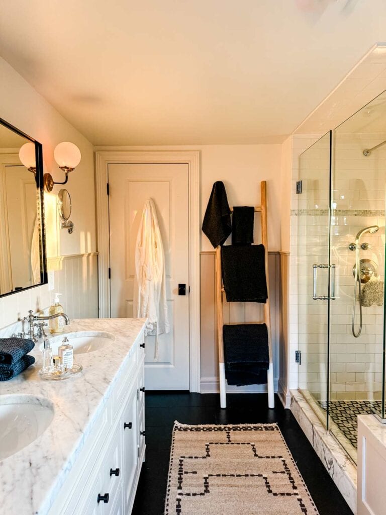 Towels on a towel ladder, glass sower. door qwith black hardware, white robe.