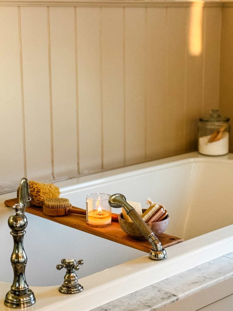 Wood tub shelf with bath items, jar with epsom salt and wood sccoop on edge of tub.