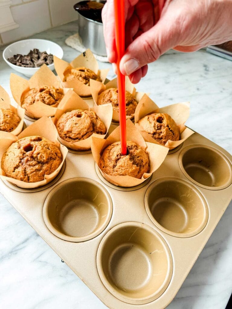 A straw is being used to make a hole in the center of each pumpkin spice muffin. The hole will be filled with molten chocolate.