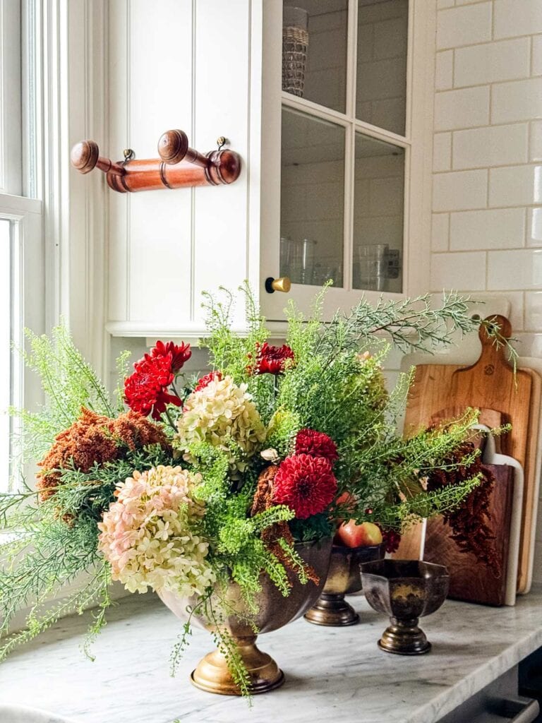 A 2 peg vintage peg hook on side of glass cabient with a large floral centerpiece on counter.