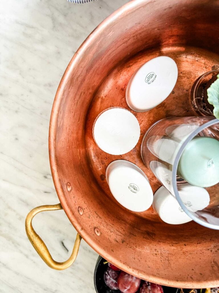 Copper pan wiht white ramekins around a glass vase with a candle.