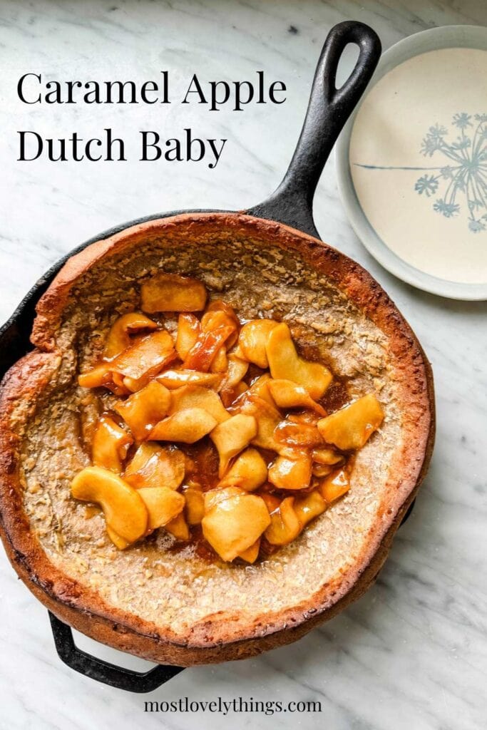 A Dutch Baby pancake is in a cast iron skillet and covered with caramelized apples. 