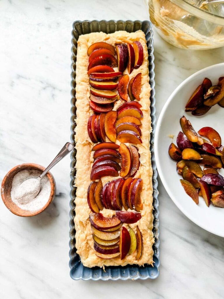 rectangular tart tin with puff pastry and uncooked plum slices arranged in rows in alternating in different directions. 