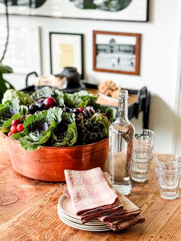 Fall centerpiee in large copper pan, clear glass bottle, glassses, napkins on a stack of plates with blue rim.