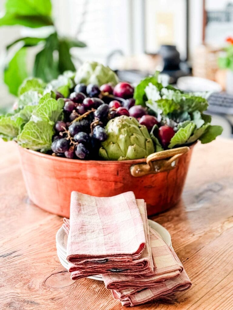 A fall centerpiece with cabbage, artichokes, grapes in large copper preserving pan.