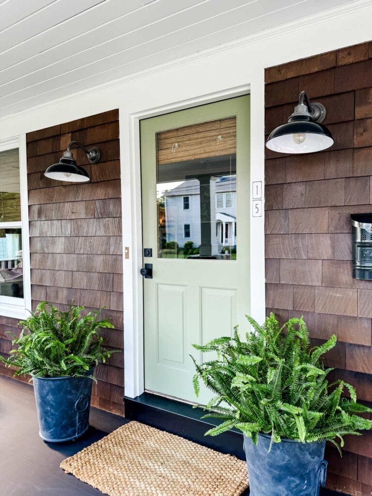 A freshly painted front door is the focal point of the porch of a Nantucket-style house.