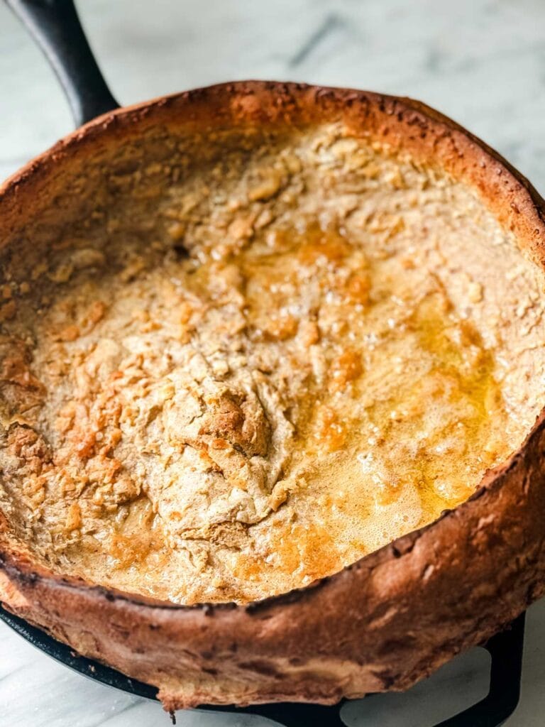 A puffy Dutch Baby pancake has baked in the oven and is ready for adding the caramelized apples.