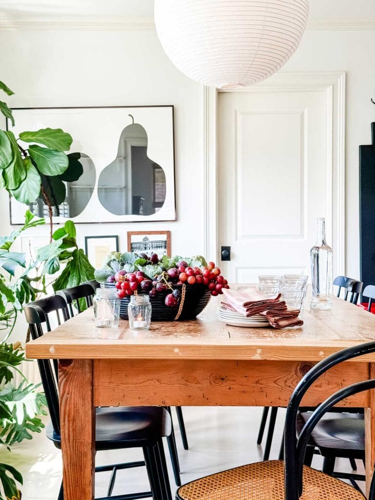 Farm table with black chairs, basket of fall plants, jars with tea light. Apple pear poster on wall in black frame. 