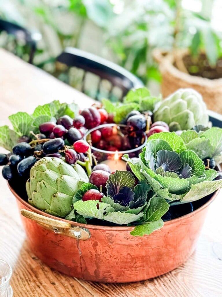 A fall centerpiece with cabbage, artichokes, grapes in large copper preserving pan.