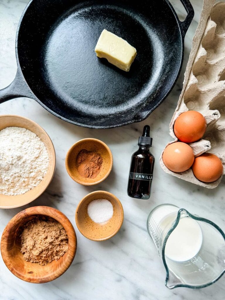 Butter is in a cast iron skillet and all the ingredients for making a Dutch Baby pancake surround the skillet.