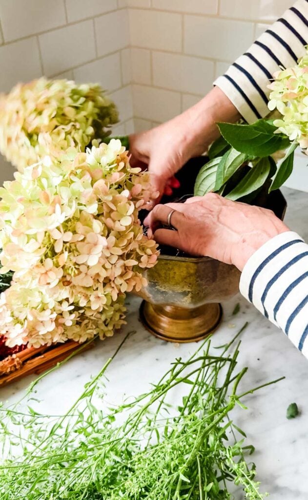 Arranging flowers in a gold vase wearing a striped shirt. 