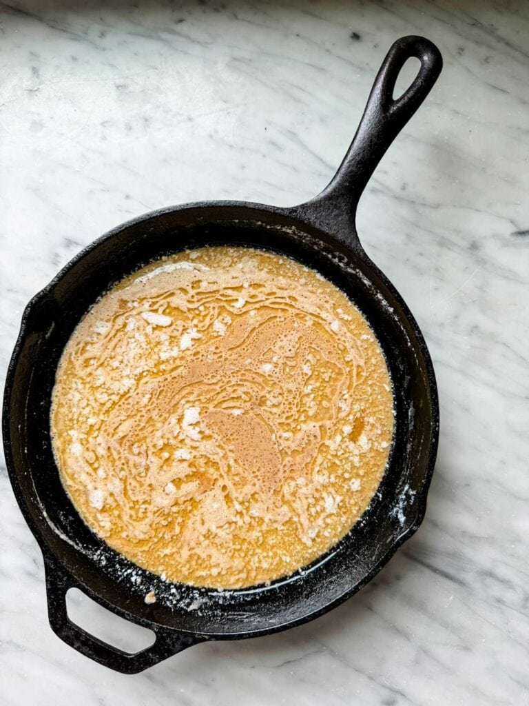 Dutch Baby pancake batter has been poured into a cast iron skillet with melted butter.