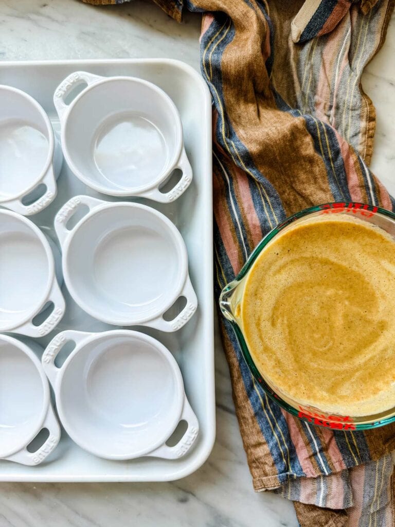 Staub mini pots in baking dish, with pumpkin mixture in glass measuring cup on stripe dish towel.