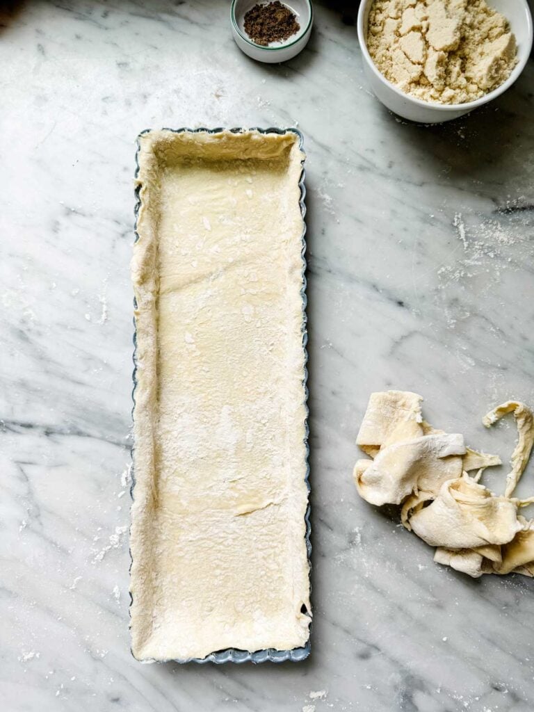 Puff pastry tart in a rectangular tin with leftover puff pastry on counter. 