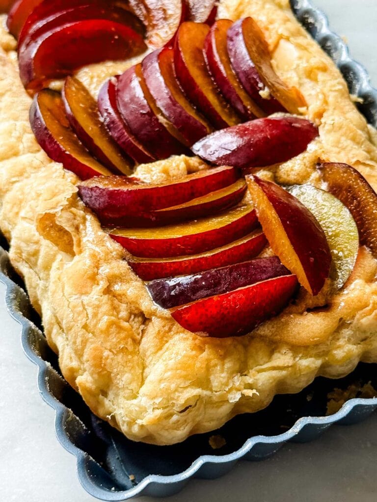 Corner angle of rectangular tart tin with puff pastry and uncooked plum slices arranged in rows. 