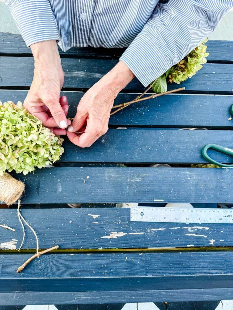 A woman is tying two hydrangea stems together to make a rustic hydrangea wreath.