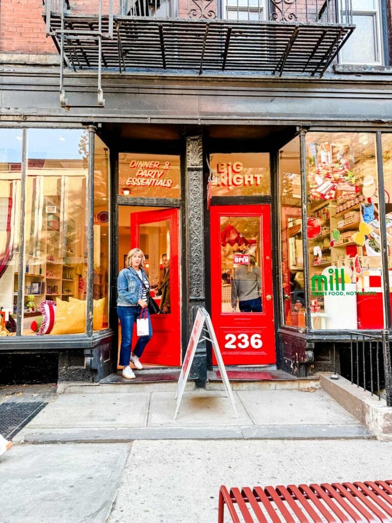 A woman is walking out of the bright red doors of Big Night in the West Village of NYC.