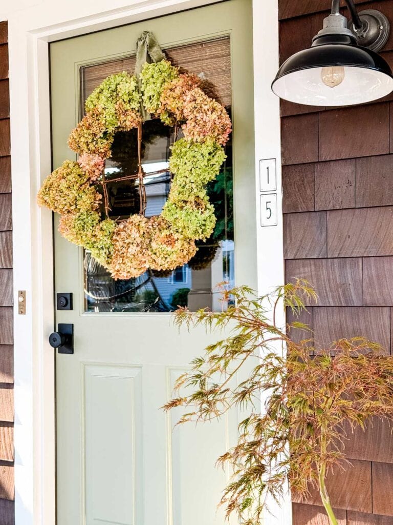 A rustic hydrangea wreath is hanging on the front door of a house. 