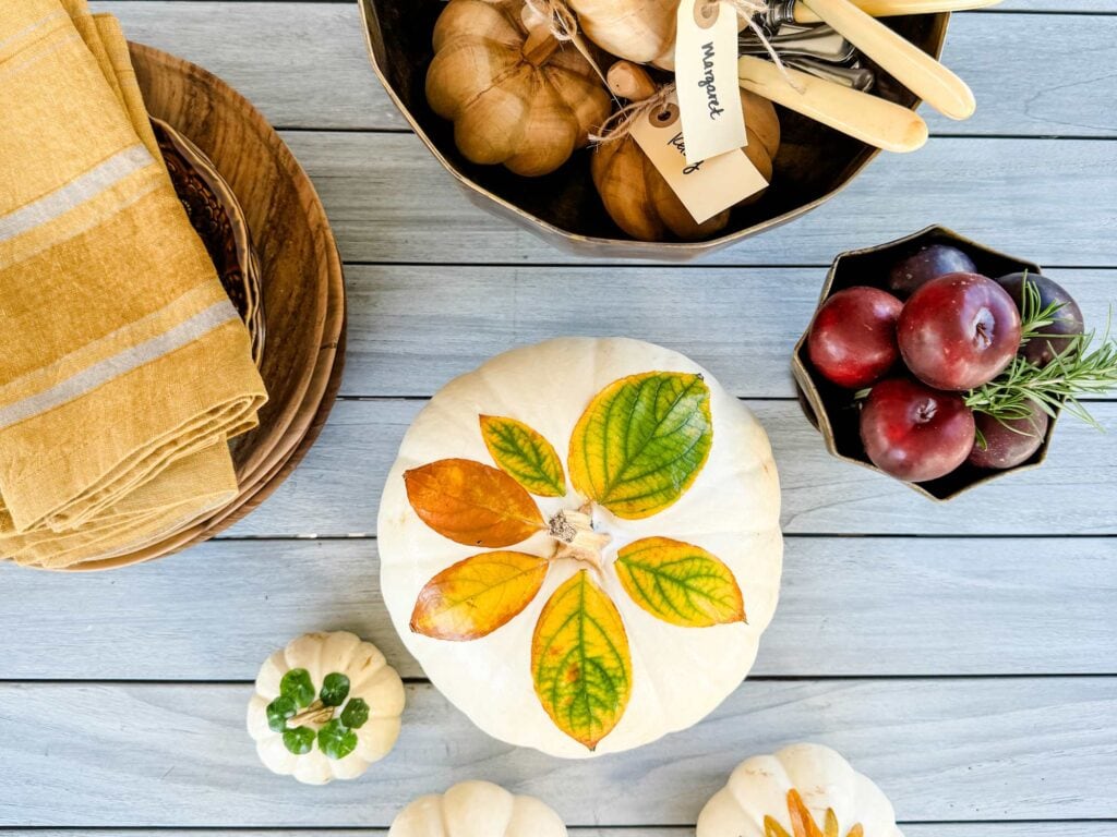 Gold strip napkins on plates, pumpkins with leaves decoupaged, plums in gold bowl, teak pumokin, kinives with bone handle in large gold bowl.