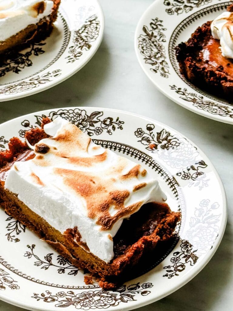 Slices of pumpkin tart with toasted meringue are served on small vintage plates.