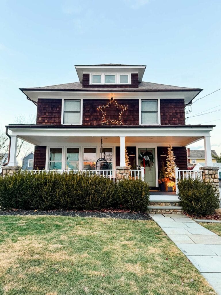 Large DIY wood star with string lights hangs on the second story of this house decorated for the holidays.