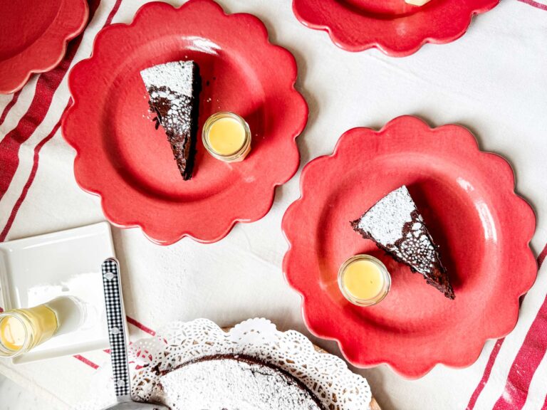 Slices of chocolate cake are on red plates with a small jar of crème anglaise.