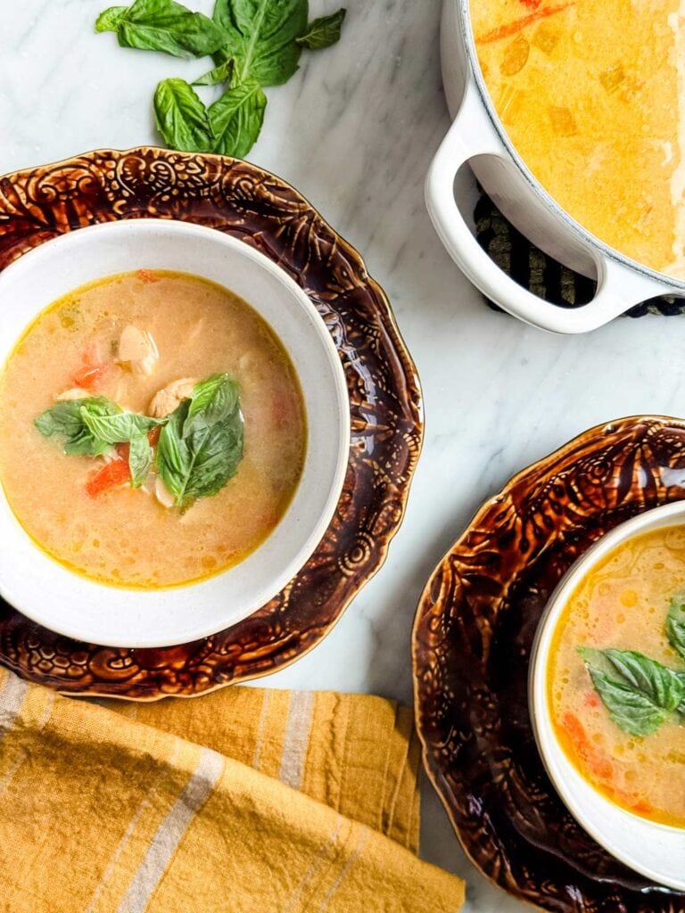 Thai coconut chicken curry soup served in white bowls on brown plates and topped with fresh basil.