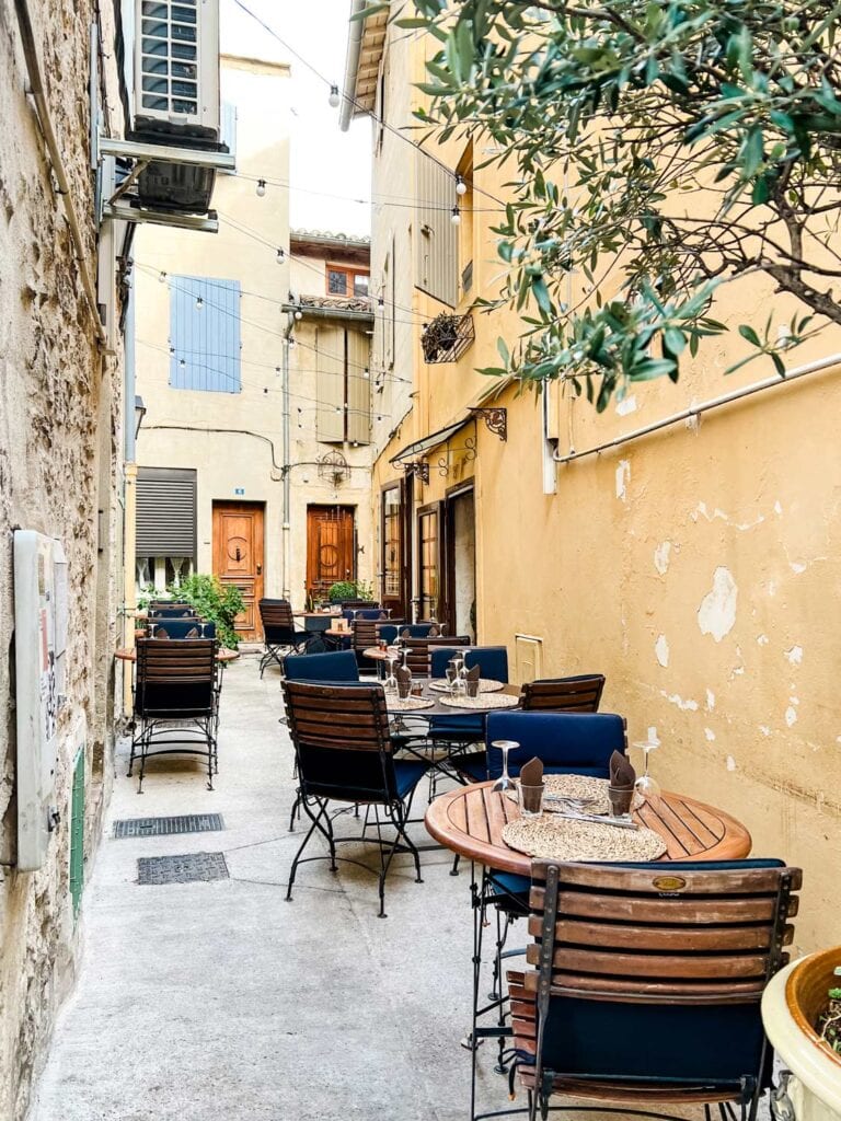 A sidestreet in Arles, France, with cafe tables for outdoor dining.