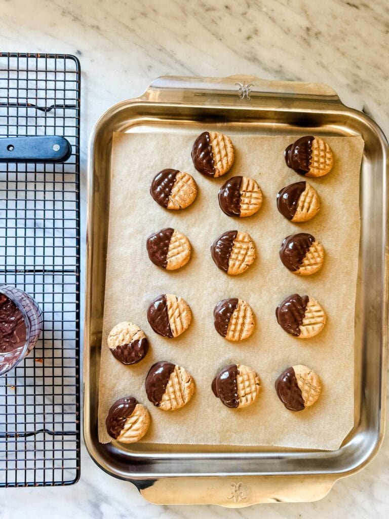 Peanut butter cookies half dipped in chocolate on cookie sheet.