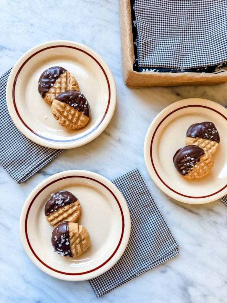 Peanut butter cookies half dipped in chocolate on small plates.