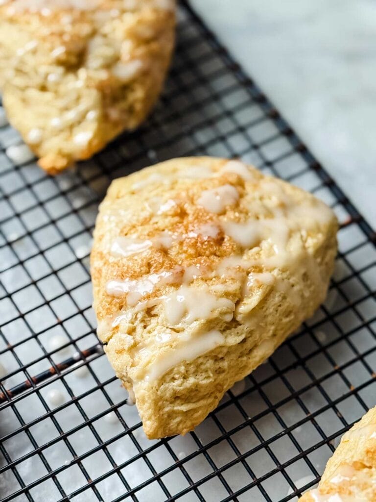 Lemon glaze on lemon scones resting on a wire cooling rack.