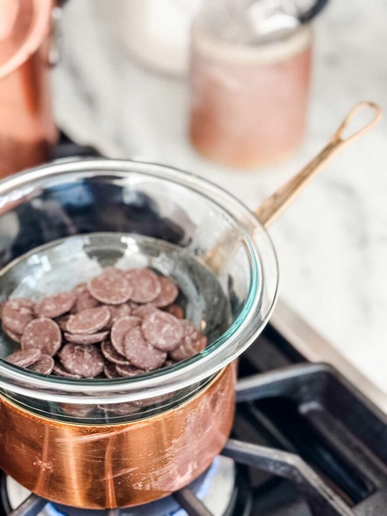 Pyrex bowl with chocolate wafers on top of copper pot on stove.