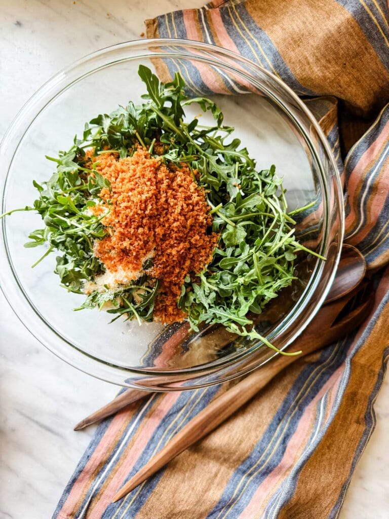 A lemon vinegarette, arugula, toasted Panko crumbs, and pecorino cheese are tossed together and placed on top of the spicy tomato beans.