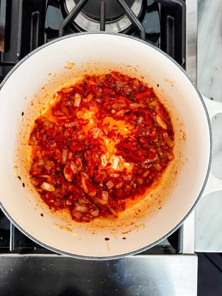 Onion, garlic, red pepper flakes, and tomato paste are caramelizing in a Dutch oven.