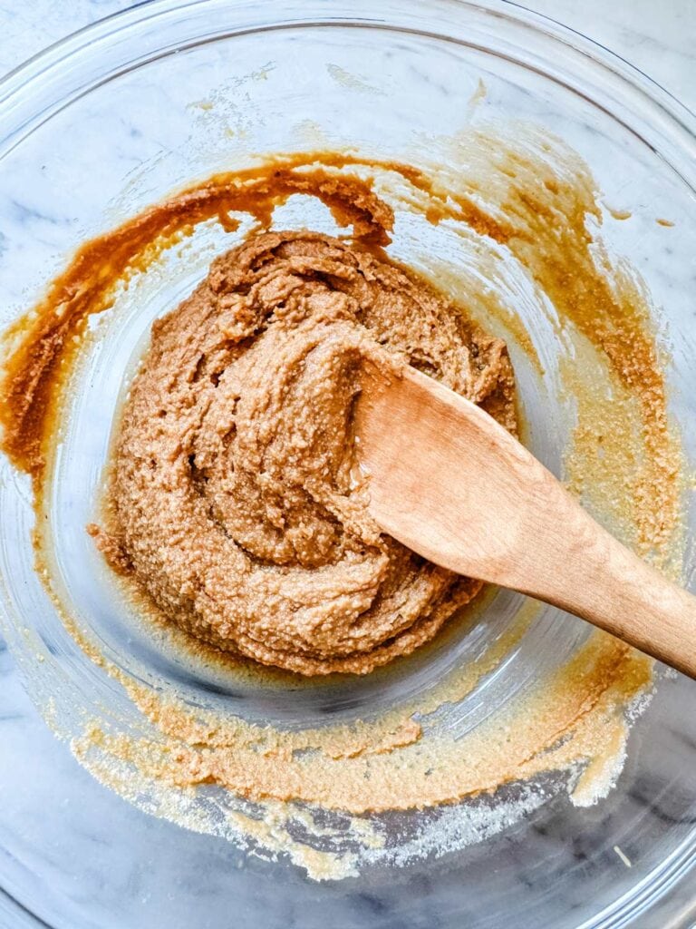 Glass bowl of peanut butter cookie dough with wood spoon.