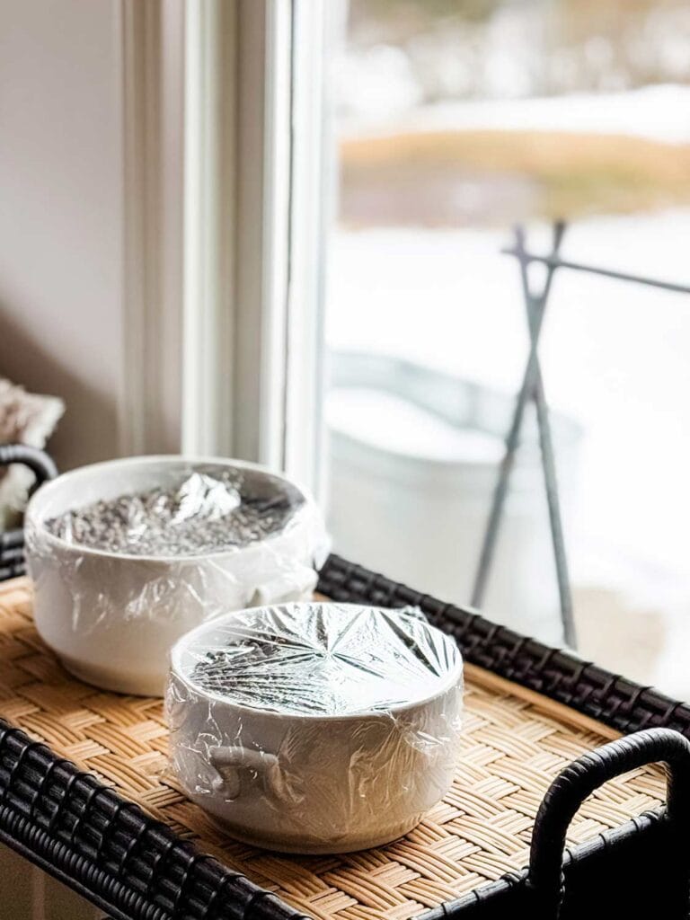 Pea seeds have been planted, watered, and covered with plastic and are sitting in front of a window.