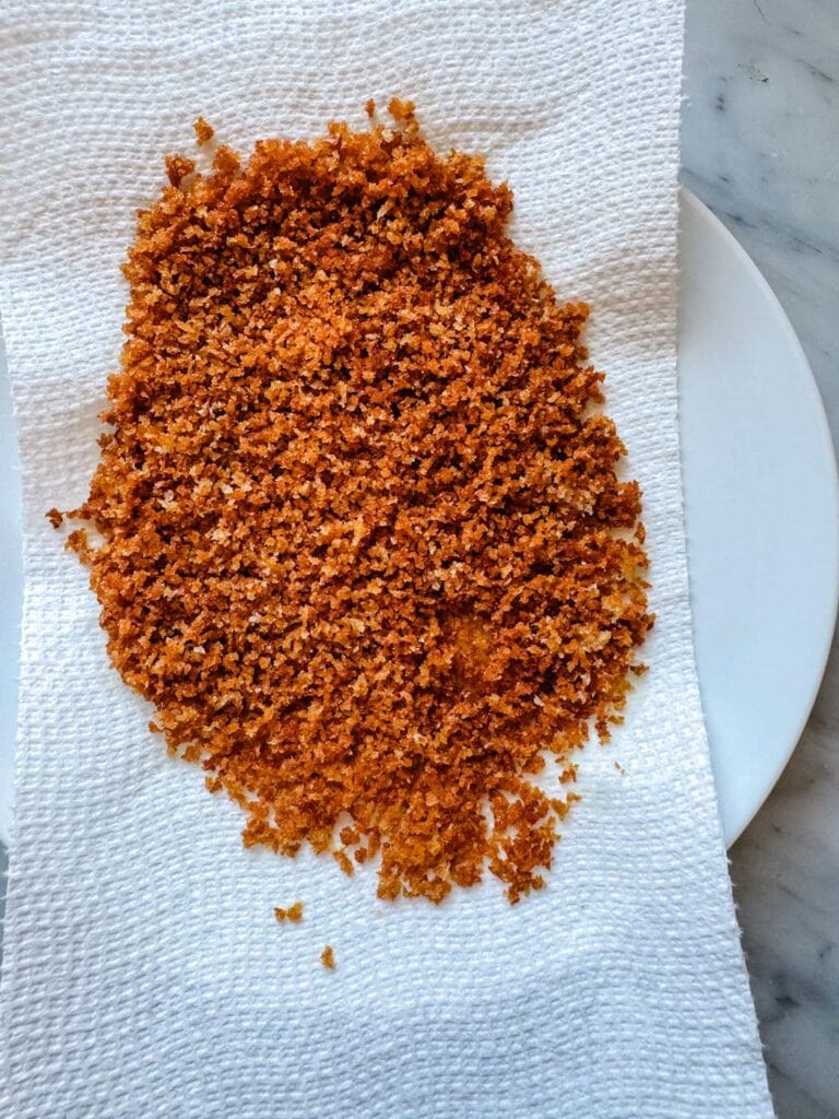 Panko crumbs have been toasted in a skillet and have been poured onto a paper towel-line plate for the oil to drain.