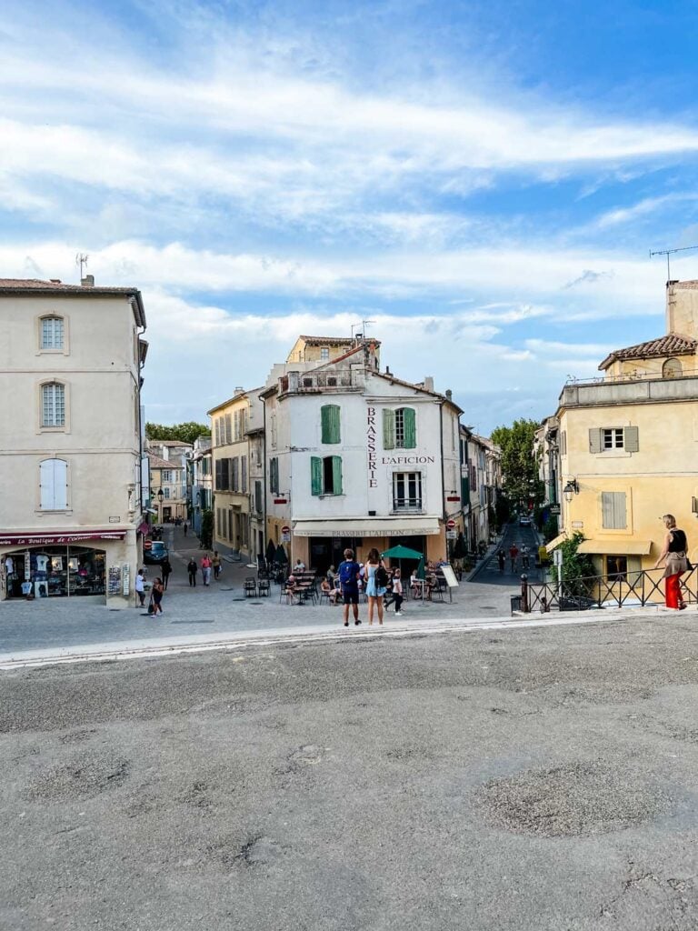 Across the street is a small cafe with outdoor seating in Arles, France.